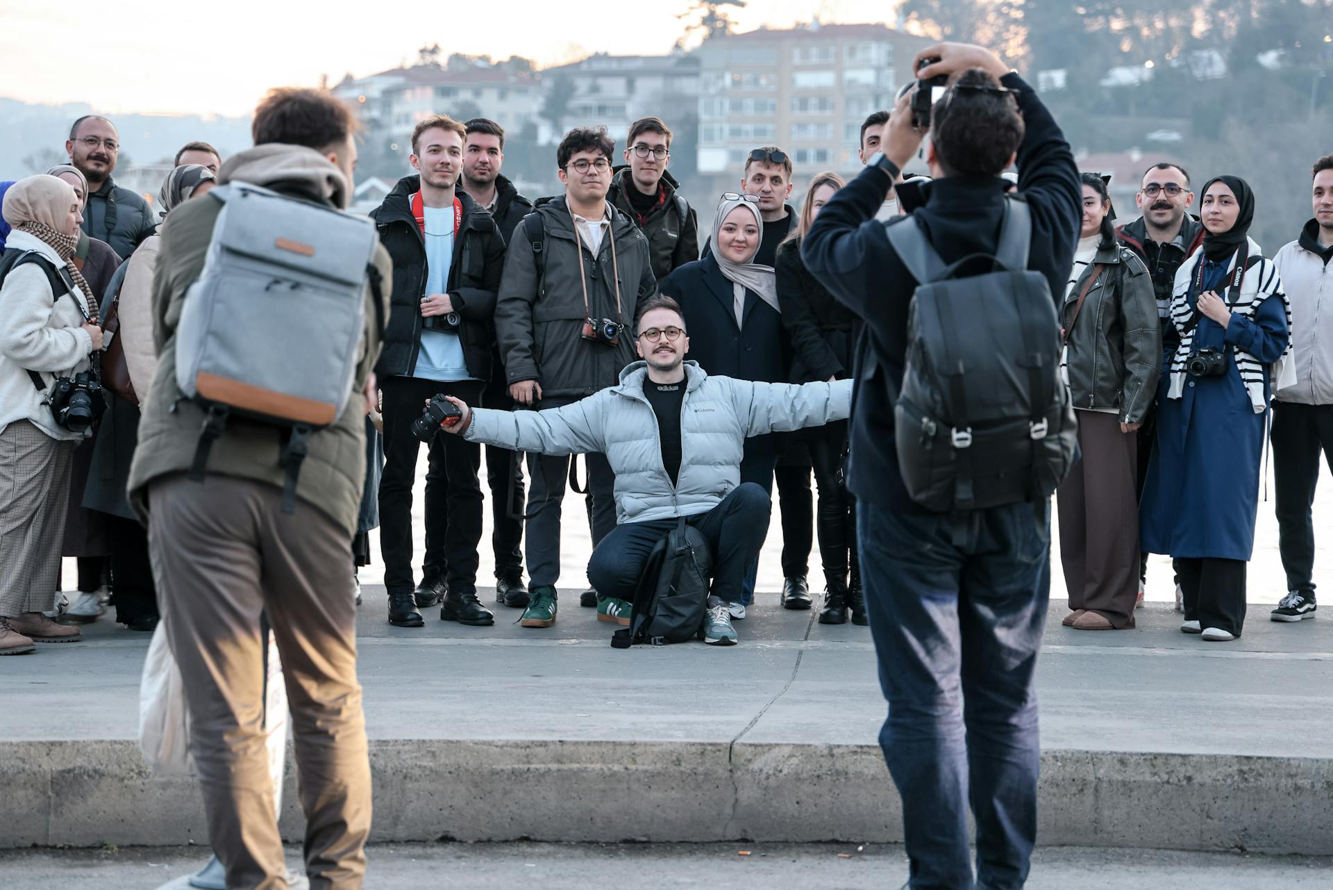 A diverse group of tourists posing for a photo outdoors by the waterside.