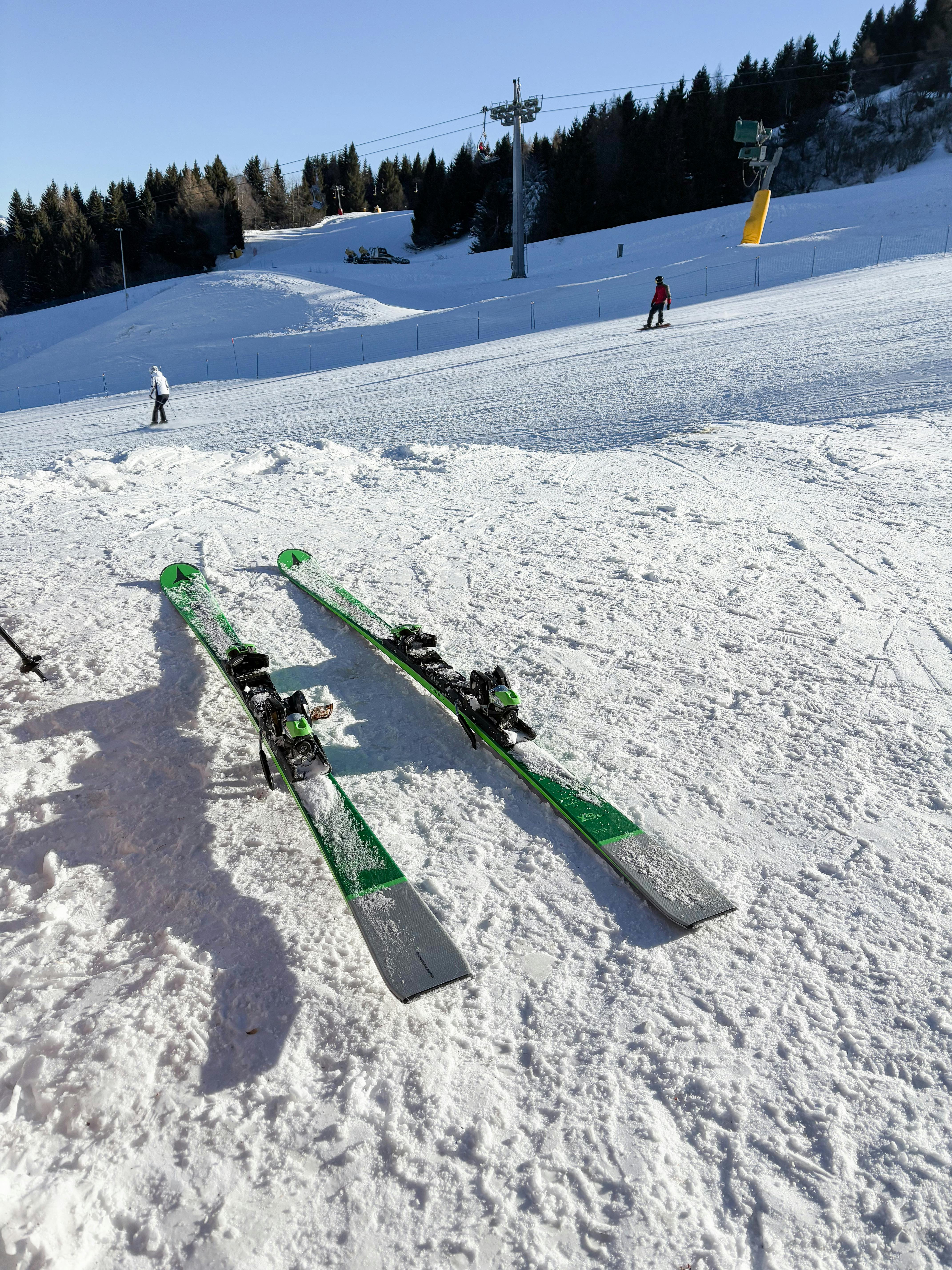 Pair of skis resting on snow with skiers in the background at a ski resort in winter.