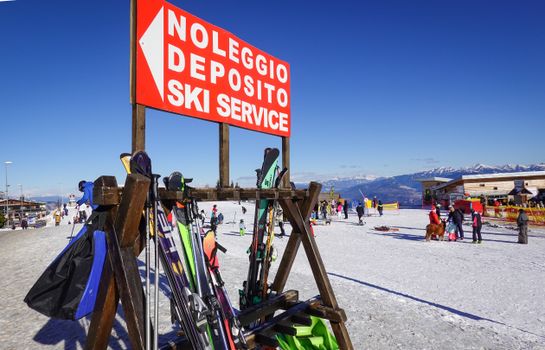 Busy ski service station with equipment and skiers in Italian Alps resort on a sunny winter day.