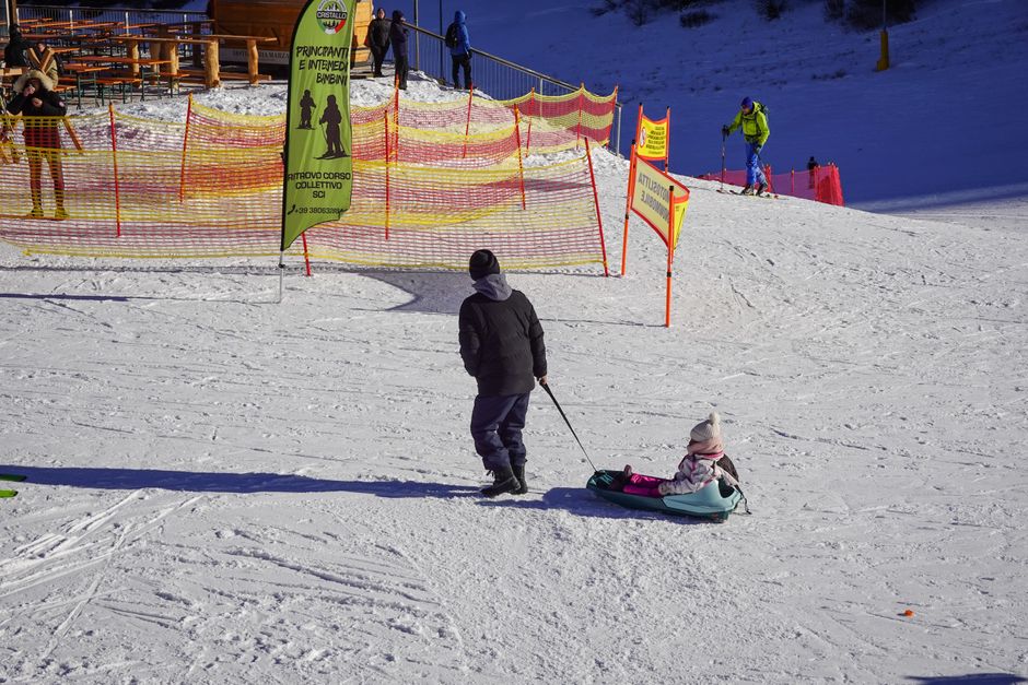 A parent pulls a child on a sled at a snowy ski resort, enjoying the winter day.
