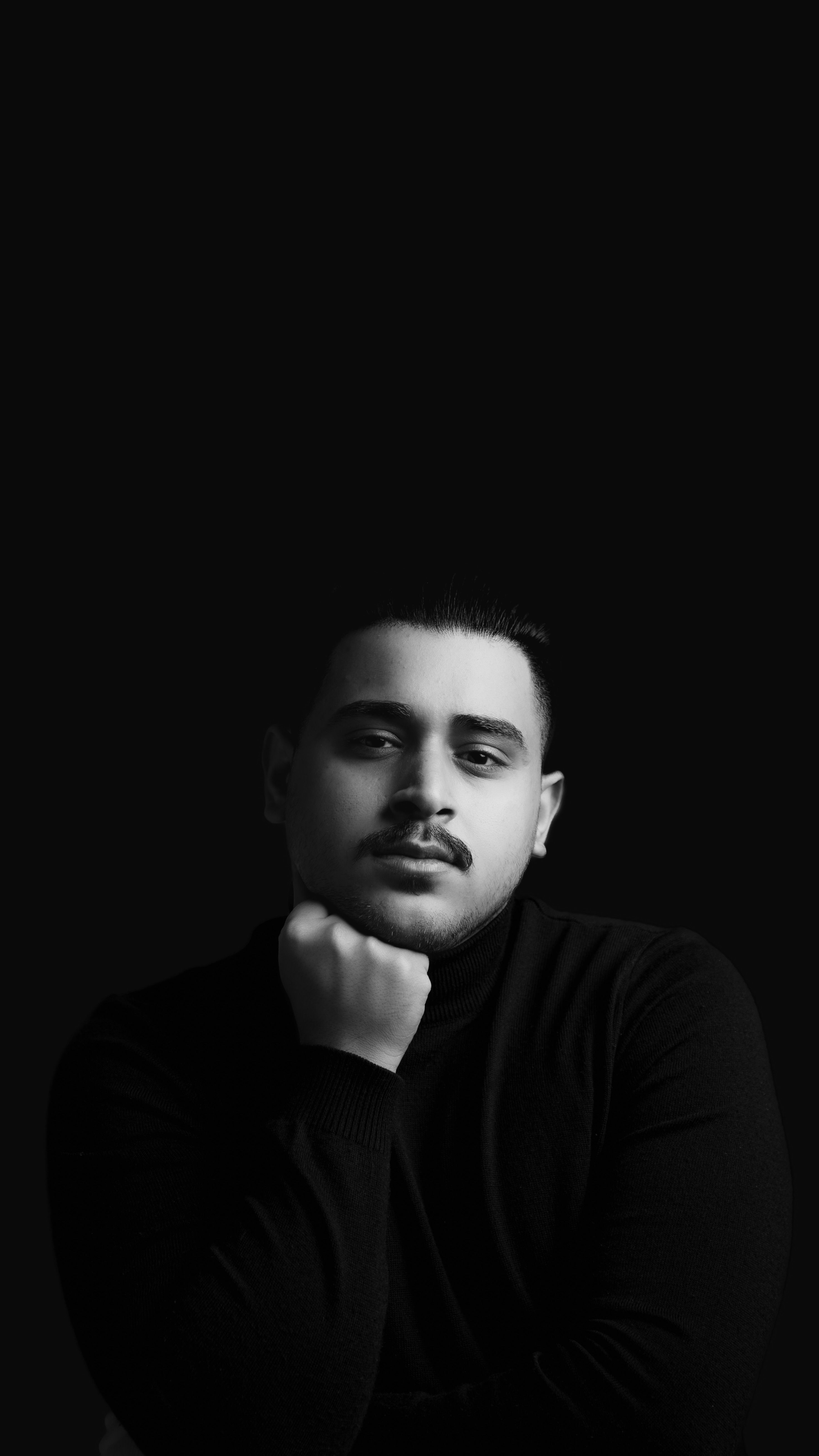 Artistic black and white portrait of a man in a thoughtful pose with a dark background.