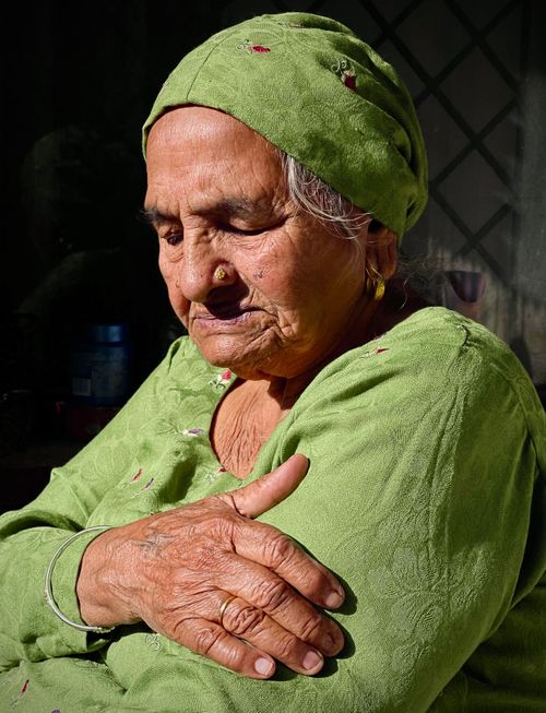 Free Portrait of an elderly woman in traditional attire, reflecting in natural sunlight. Stock Photo