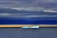 日落时分，一座孤寂的冰山漂浮在平静的海面上，云层清晰可见