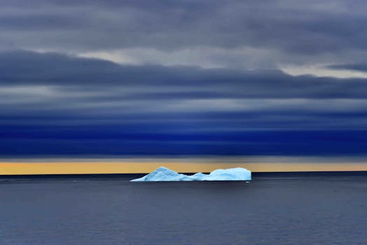 日落时分，一座孤寂的冰山漂浮在平静的海面上，云层清晰可见
