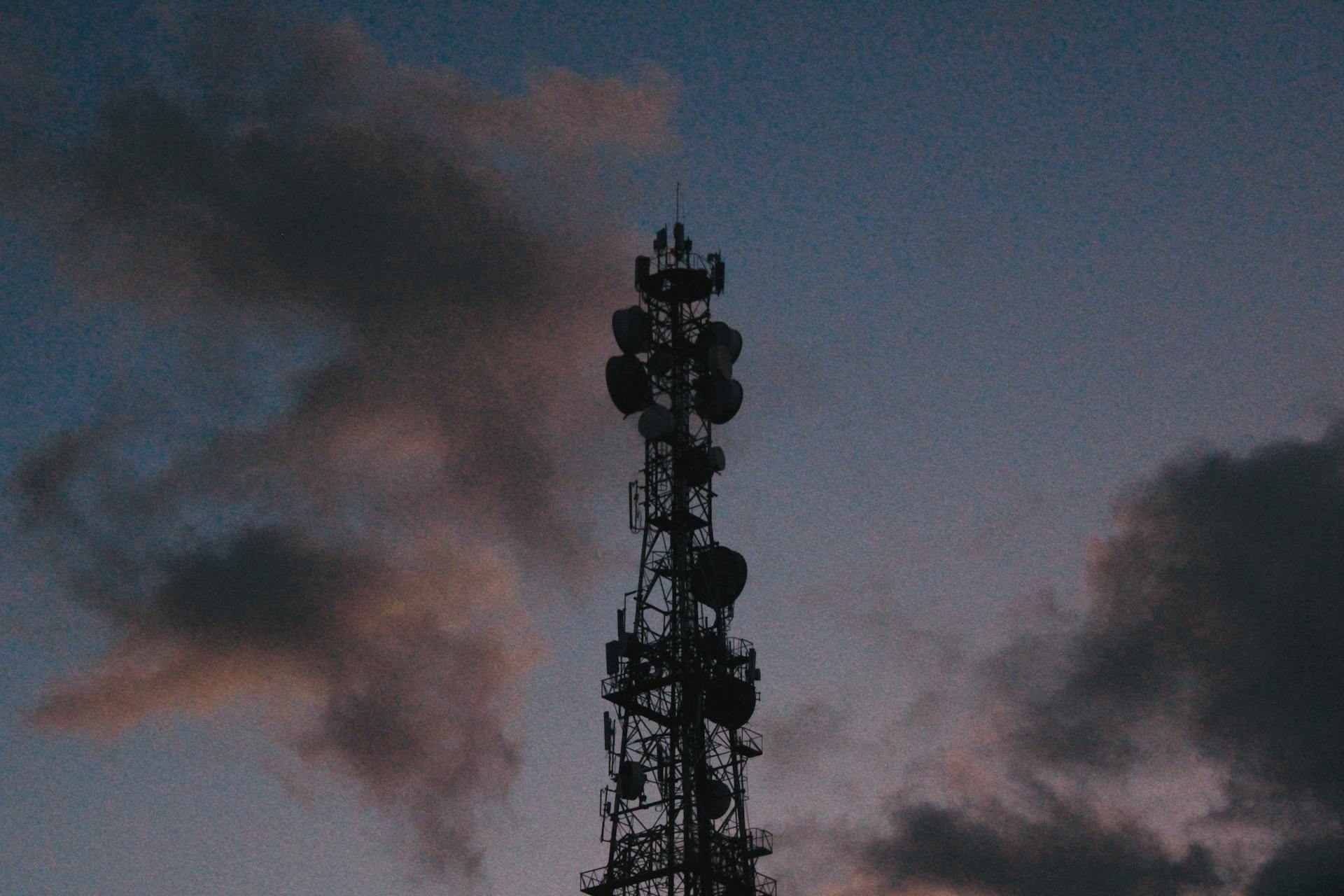 Silhouette of a telecommunications tower against a vibrant twilight sky with clouds.