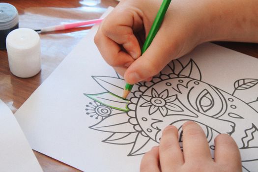 A child coloring a mandala art with a green pencil, highlighting creativity.