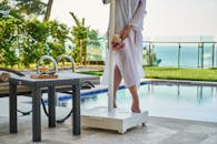 一名身穿白裙的女子，手捧鲜花，在海景映衬下，静立于泳池边