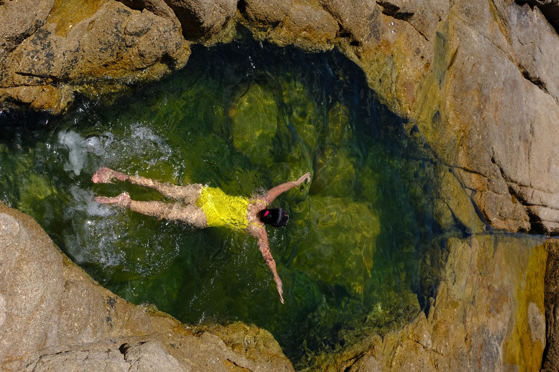 An aerial view of a woman swimming in a natural rock pool in Phú Yên, Vietnam.