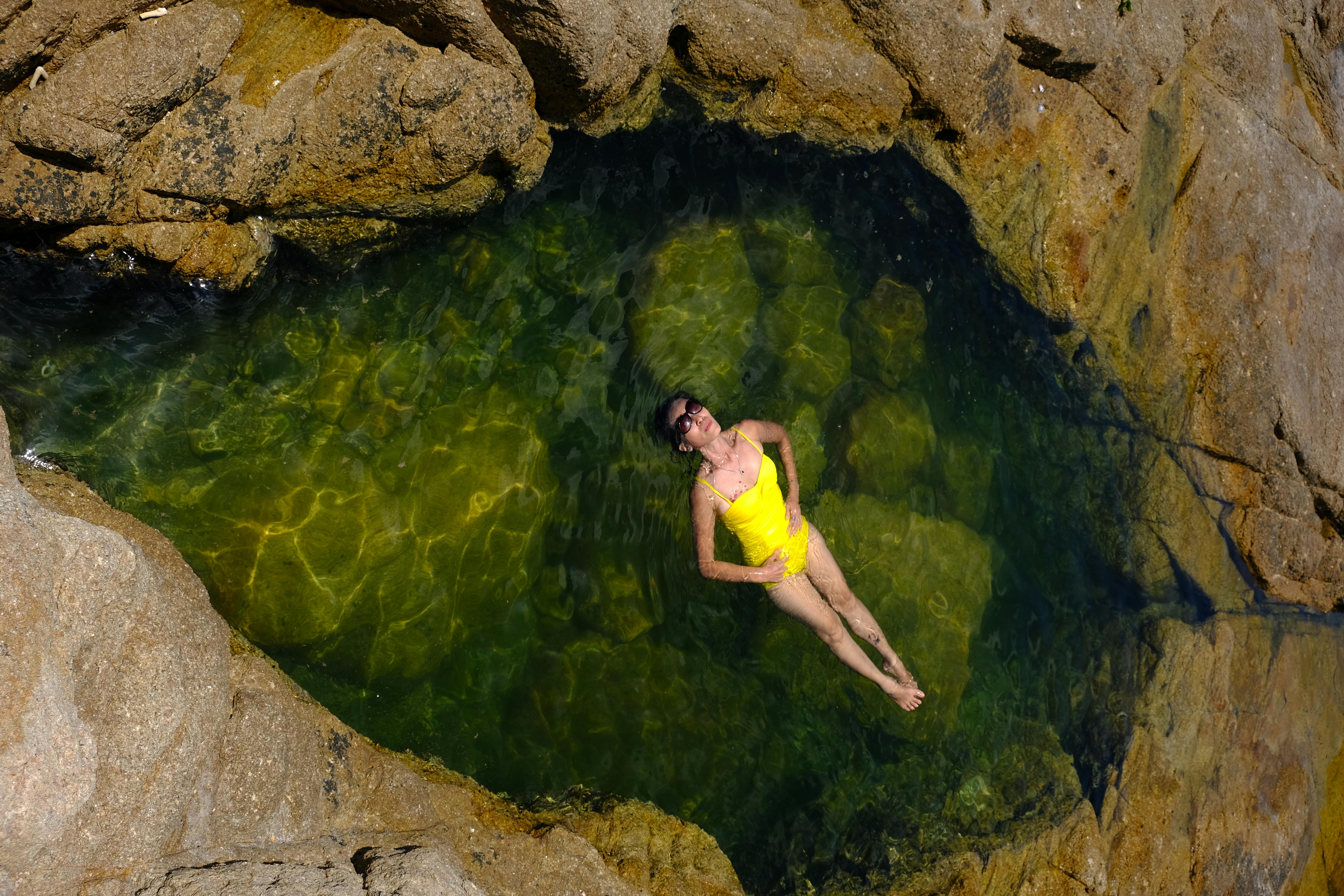 A woman in a yellow swimsuit floating in a natural rock pool in Phú Yên, Vietnam.