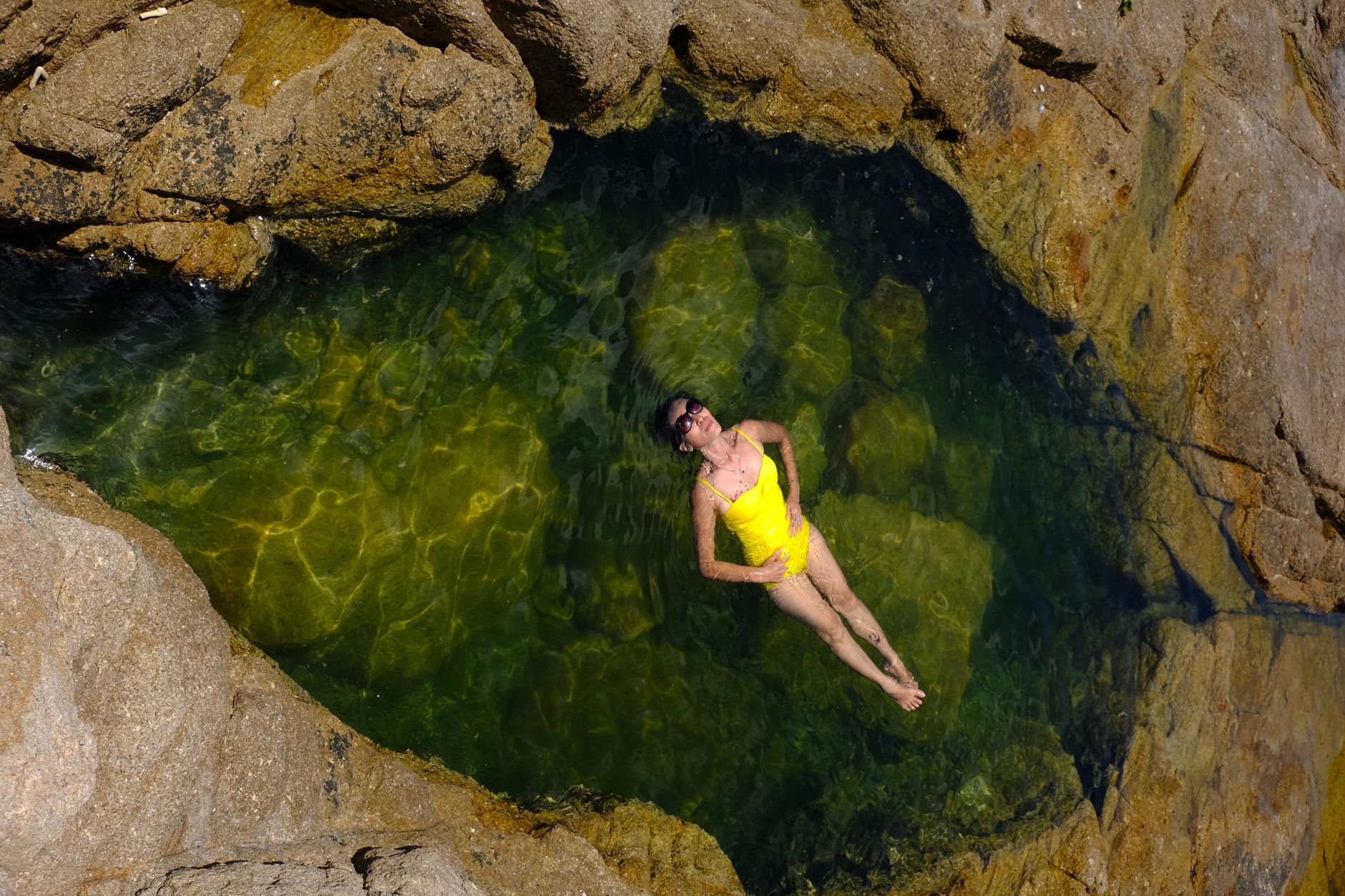 A woman in a yellow swimsuit floating in a natural rock pool in Phú Yên, Vietnam.