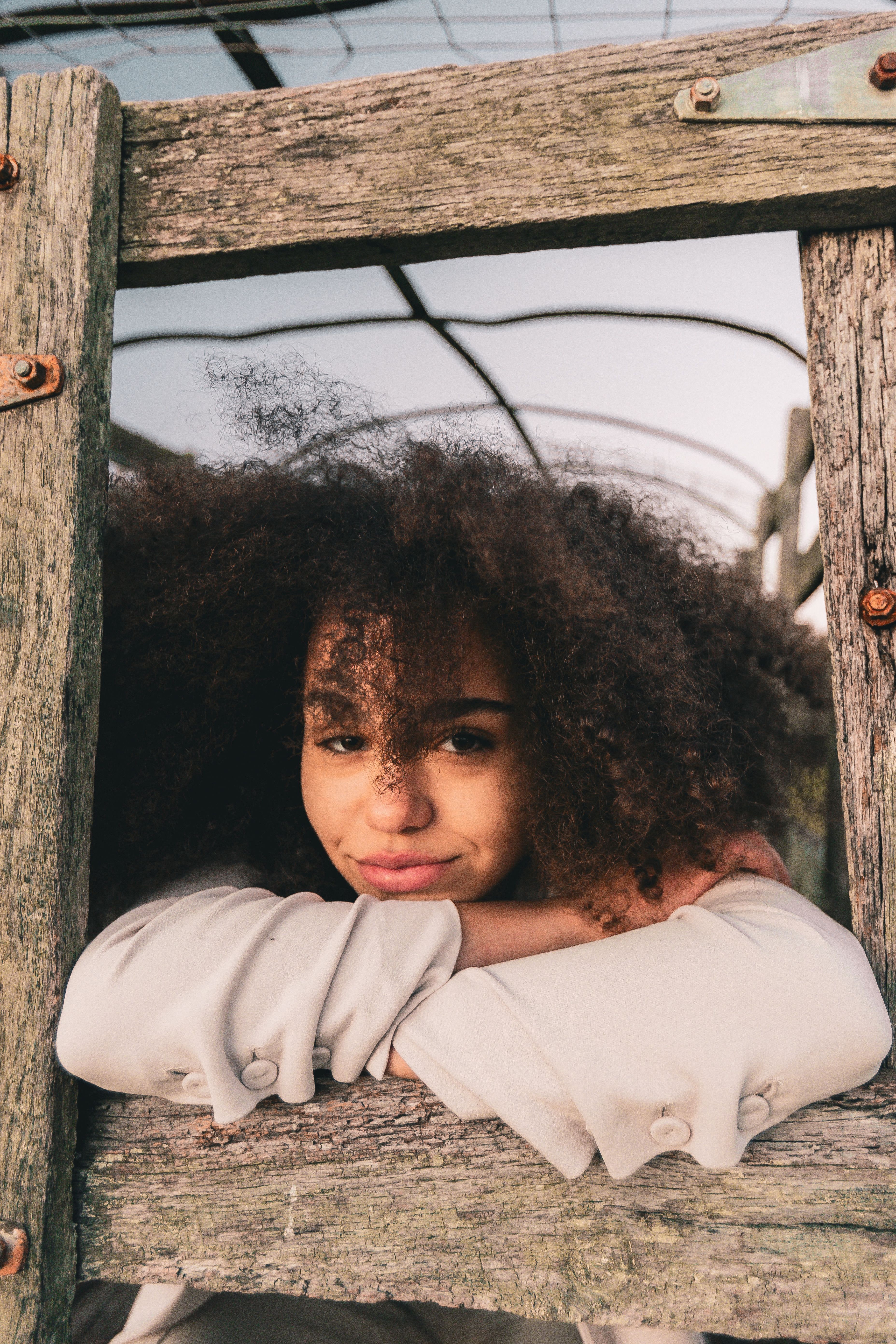 young-woman-with-curly-hair-leaning-on-rustic-fence-free-stock-photo