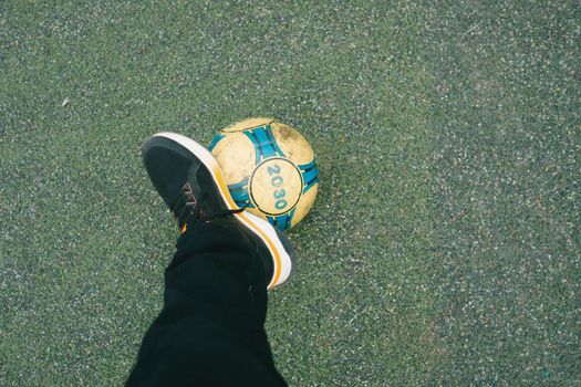 An outdoor image of a soccer player balancing a ball on their foot on grass.