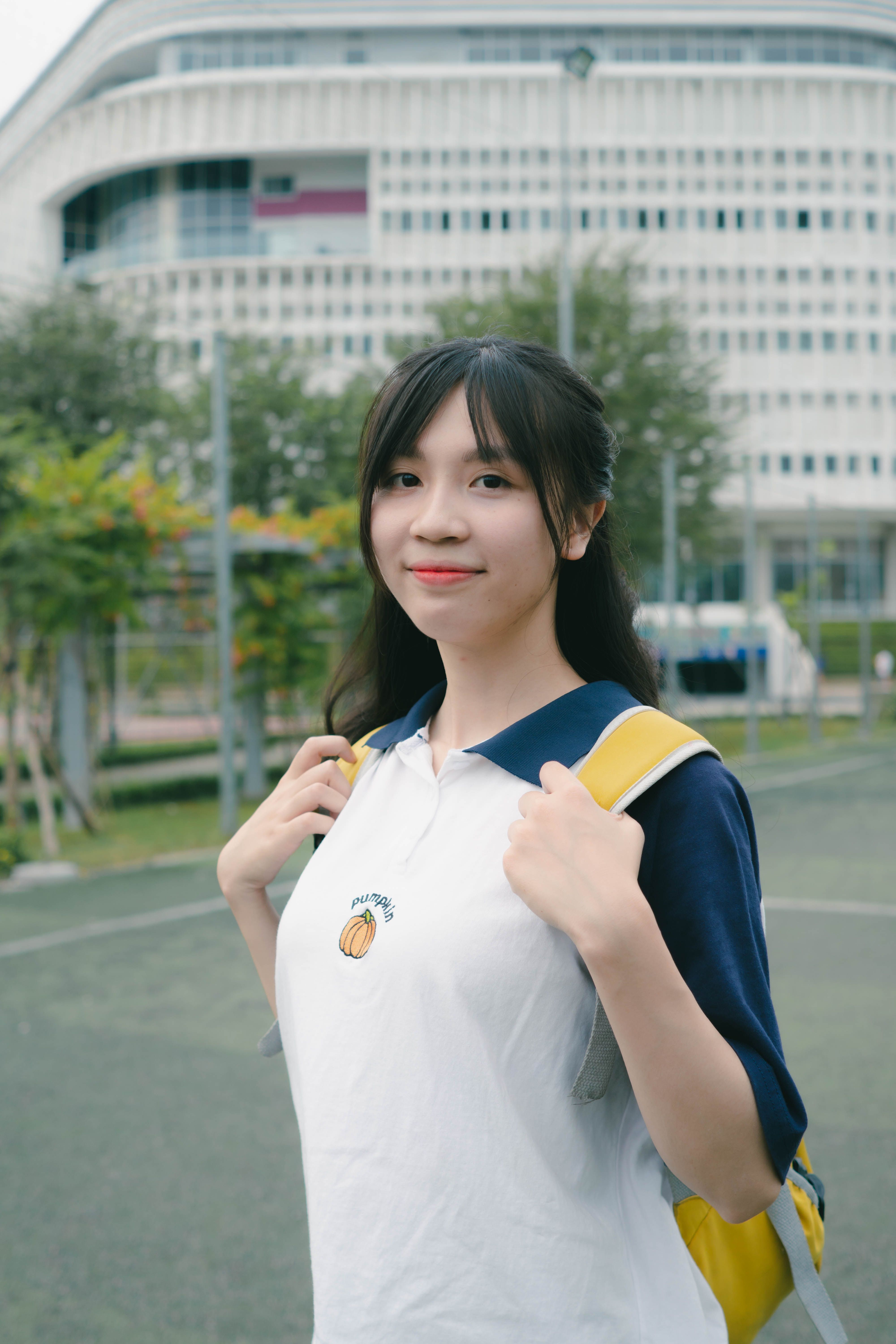 Portrait of a young woman in casual attire with a backpack, standing outdoors near a modern building.