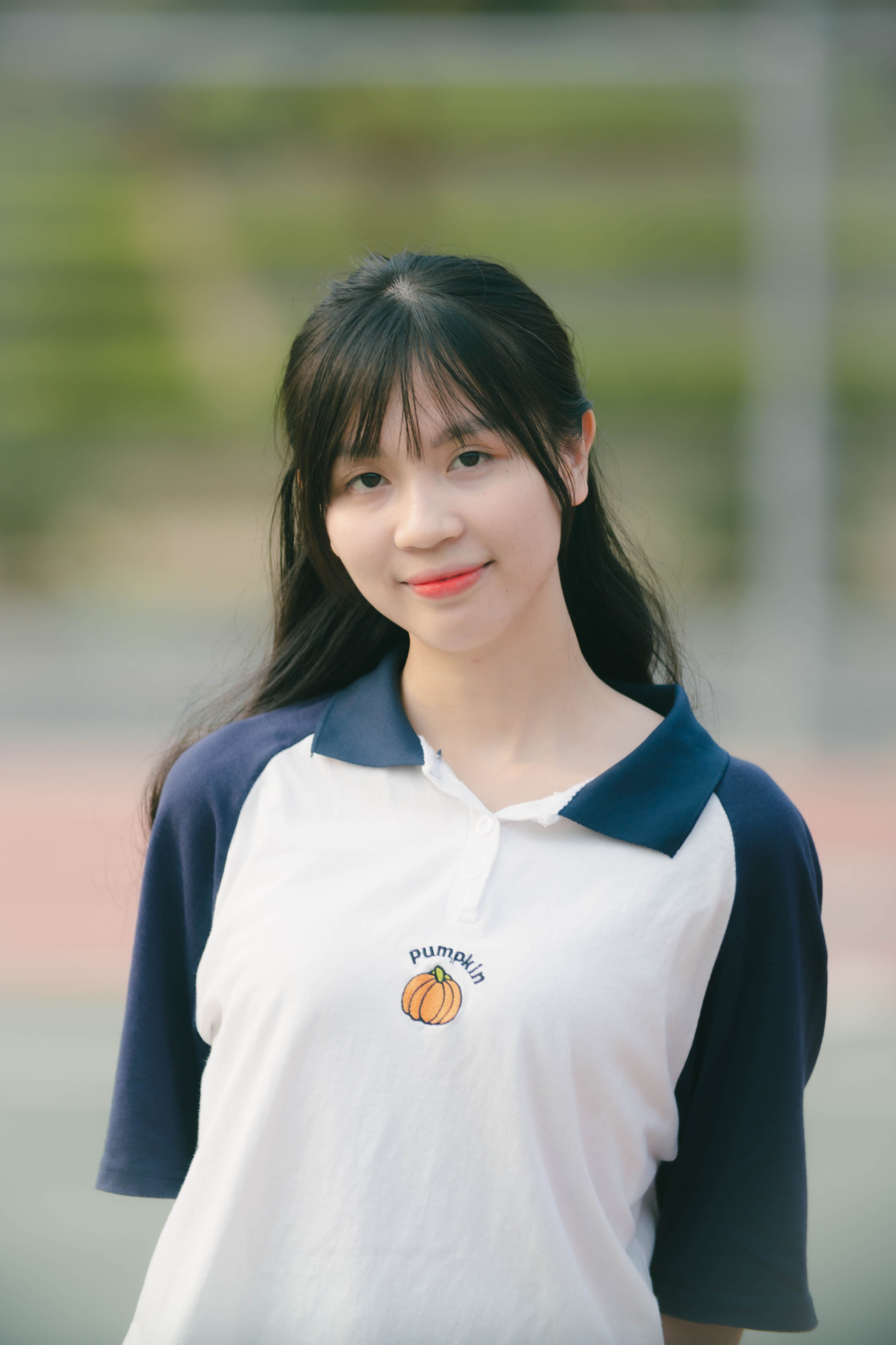 Young woman in a white and blue shirt outdoors, smiling gently.