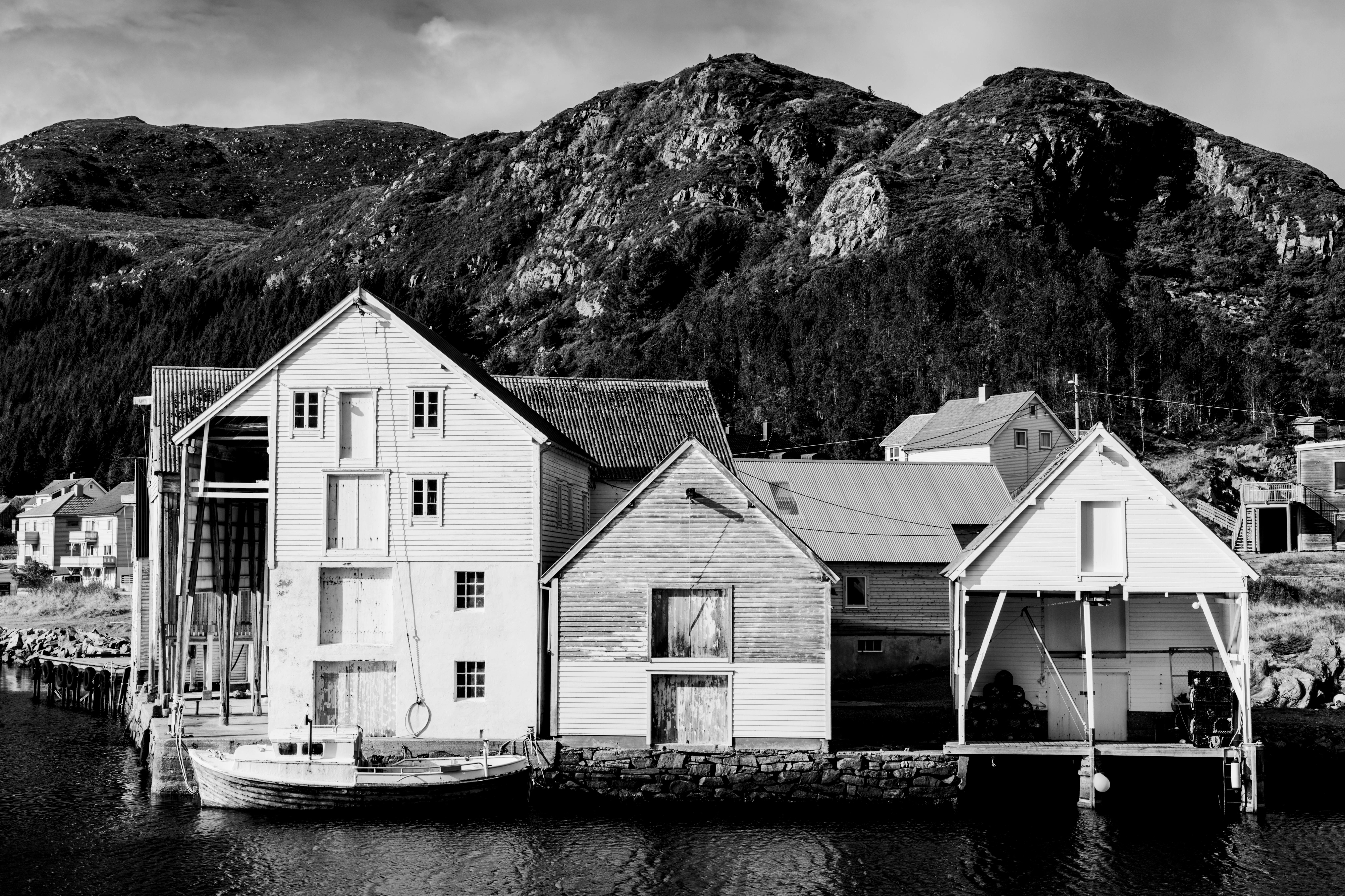 Black and white photo of a serene Nordic harbor with rustic houses and mountain backdrop.