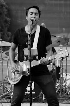 Musician passionately playing guitar and singing on stage during an outdoor rock concert.