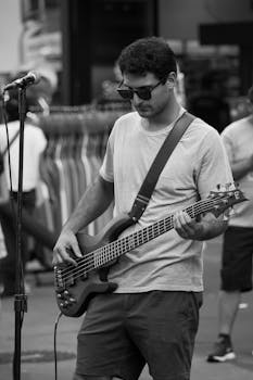 Monochrome image of a street musician playing bass guitar outdoors.