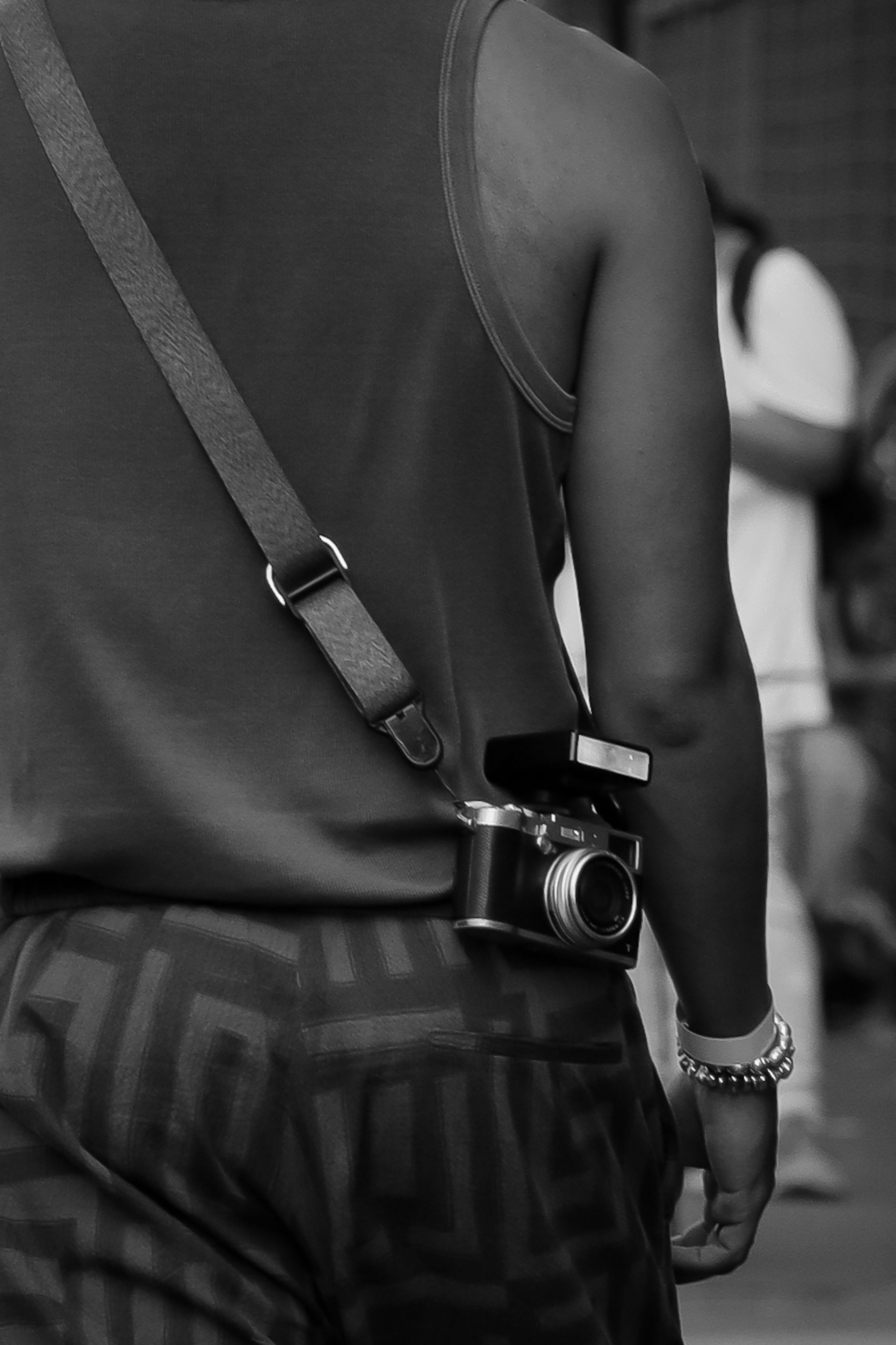 A person carrying a vintage camera, captured in a black and white street setting.