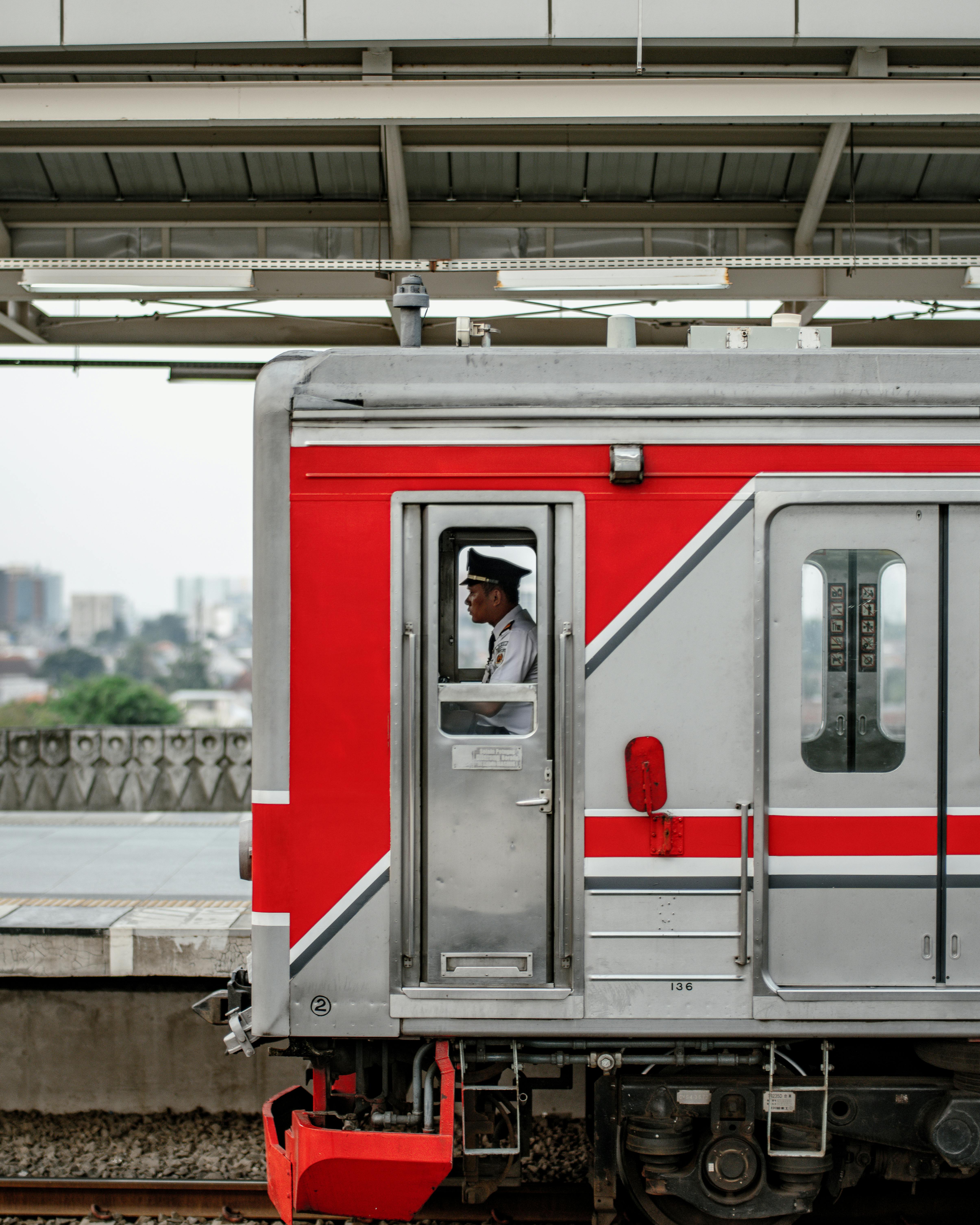Side view of red train with conductor at Jakarta station, Indonesia.