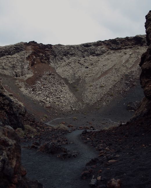 A striking volcanic landscape featuring rugged lava rocks and a barren crater under a cloudy sky.