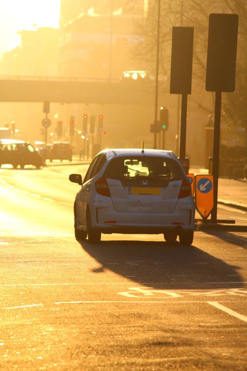 Free Sunlit urban street scene with cars, traffic lights, and a morning glow. Stock Photo
