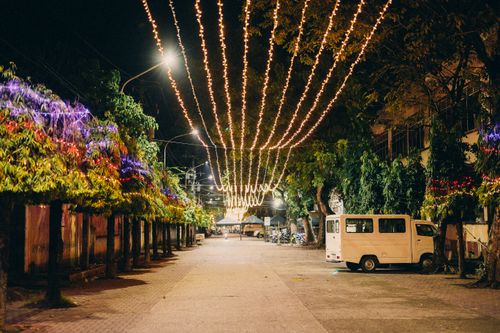 Free A night scene of a decorated street with hanging string lights and trees, creating a festive atmosphere. Stock Photo