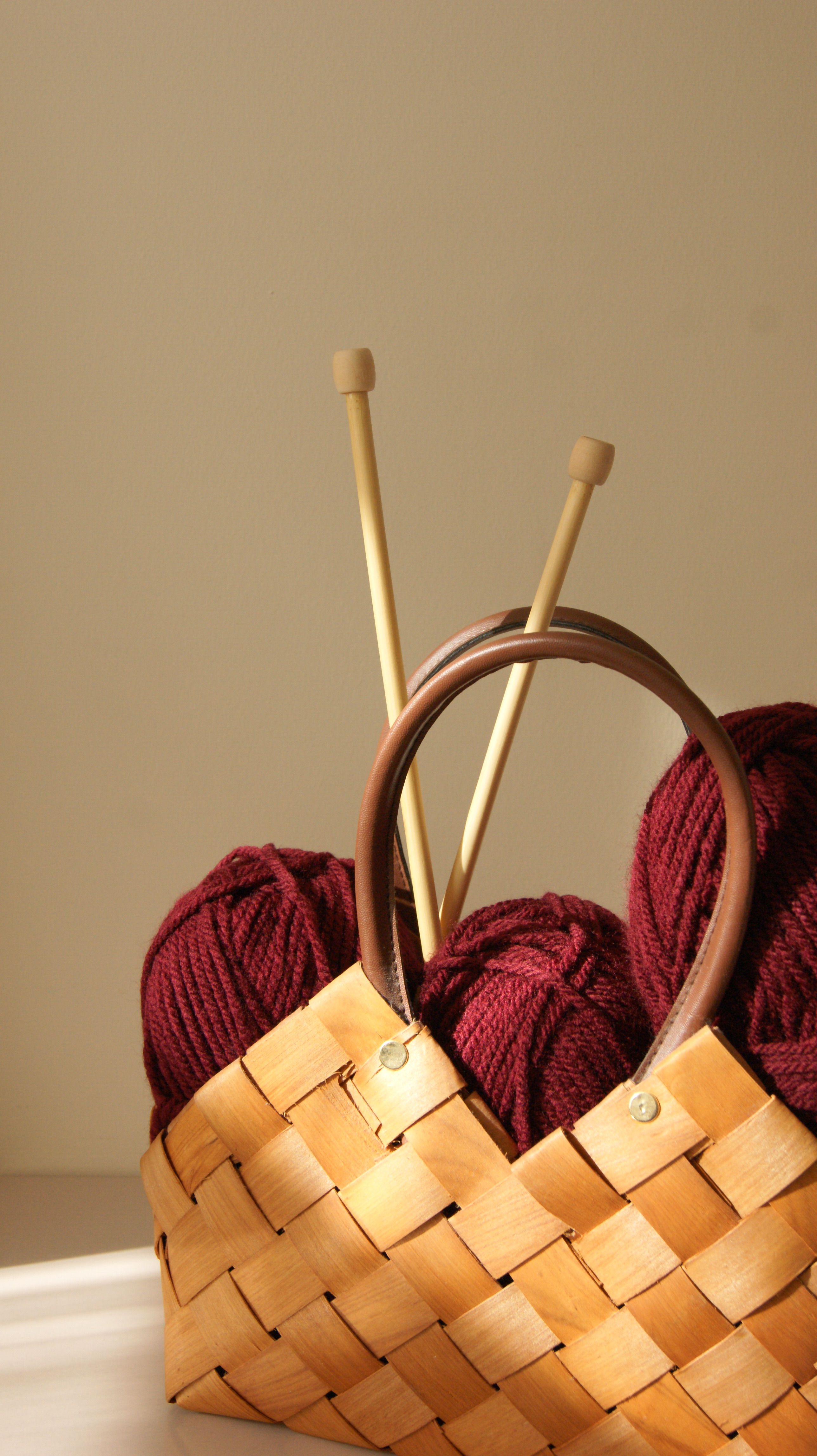 Warm maroon yarn and knitting needles in a wicker basket under soft lighting.