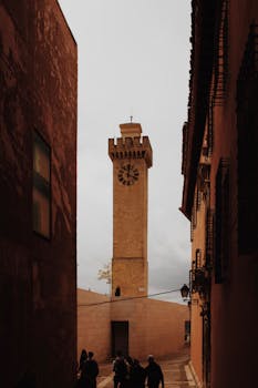 A charming alleyway leading to a historic clock tower in Cuenca, Spain.