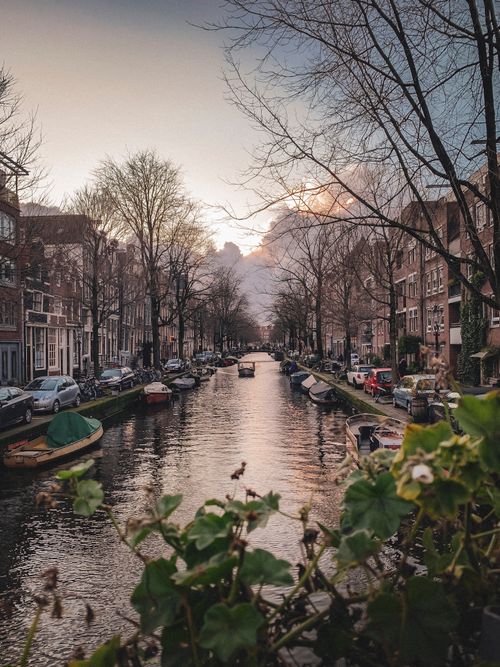 Free Scenic view of an Amsterdam canal with historic architecture and boats at sunset. Stock Photo