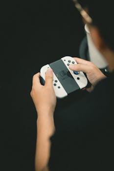 Hands holding a modern game controller against a dark background. Perfect for gaming content.