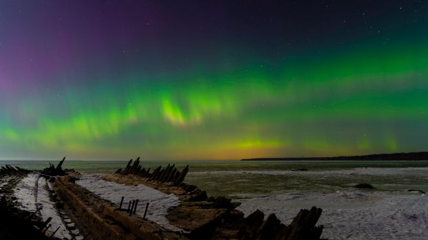 Captivating view of the Aurora Borealis illuminating the night sky over a frozen shoreline with visible starry sky.