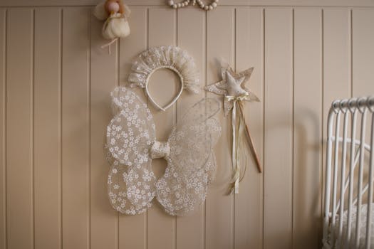 Delicate fairy costume with wings and princess wand hanging on a beige wall, perfect for a nursery.