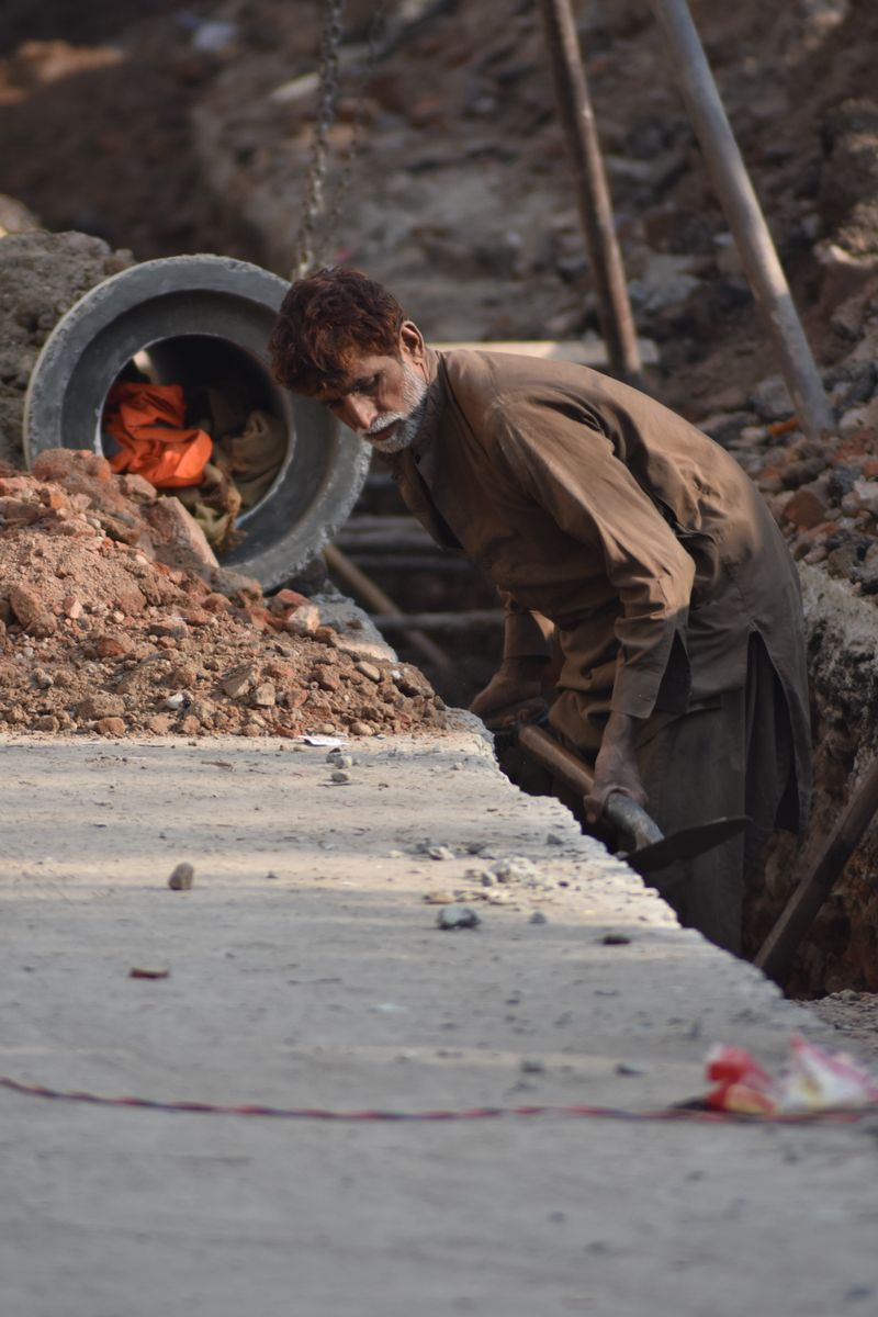 Construction worker inspecting an underground pipe installation