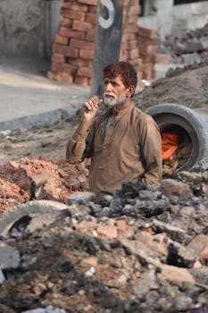 Elderly man working at a construction site amidst bricks and rubble, showcasing hard labor.