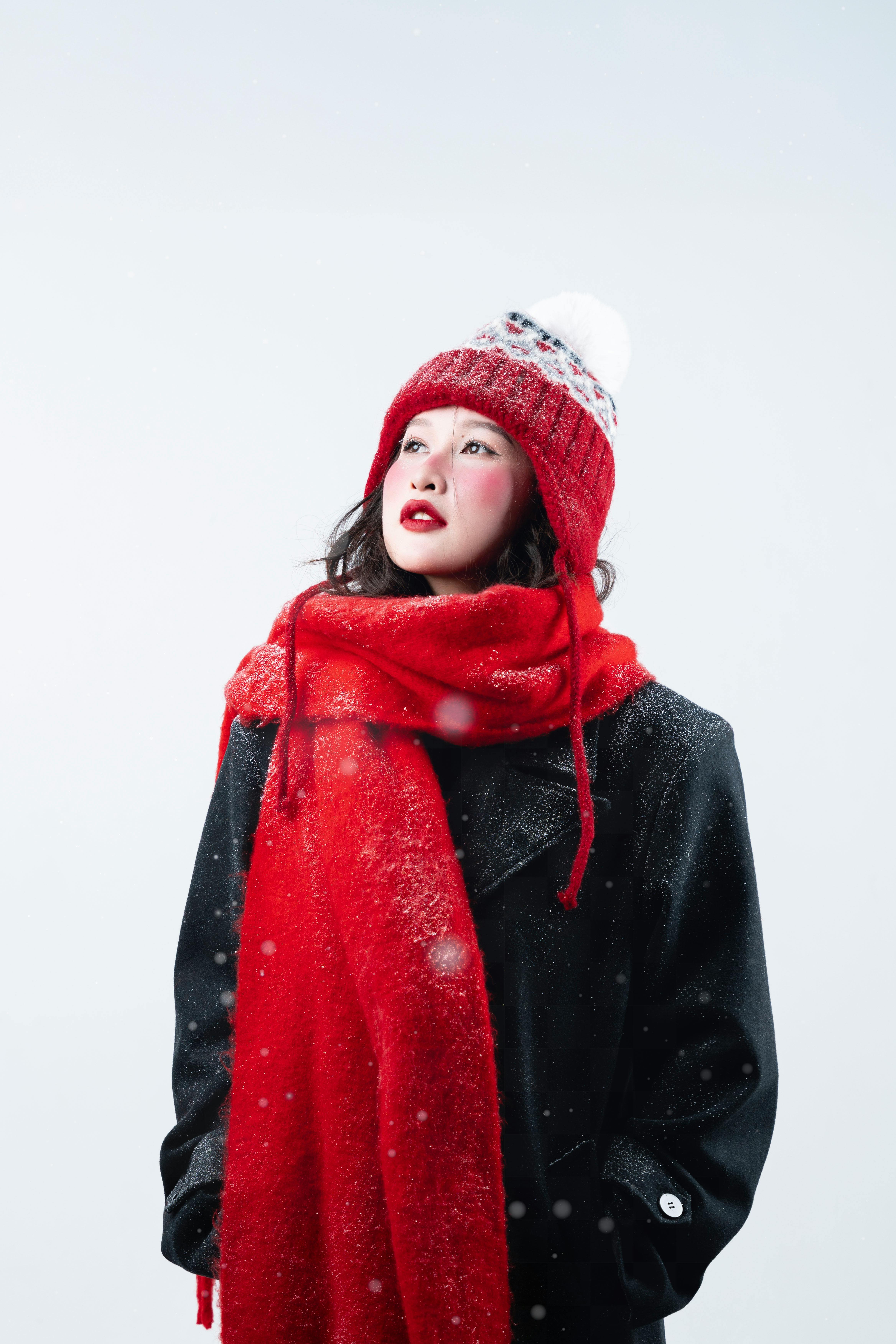 Confident woman in winter clothing with red scarf and hat, looking upward.