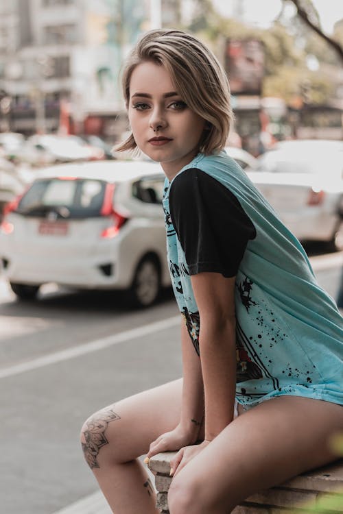 Selective Focus Photo of Woman in Teal and Black T-shirt Sitting on Concrete Edge