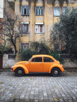 Vintage orange Volkswagen Beetle car parked on a cobblestone street in front of a rustic building.