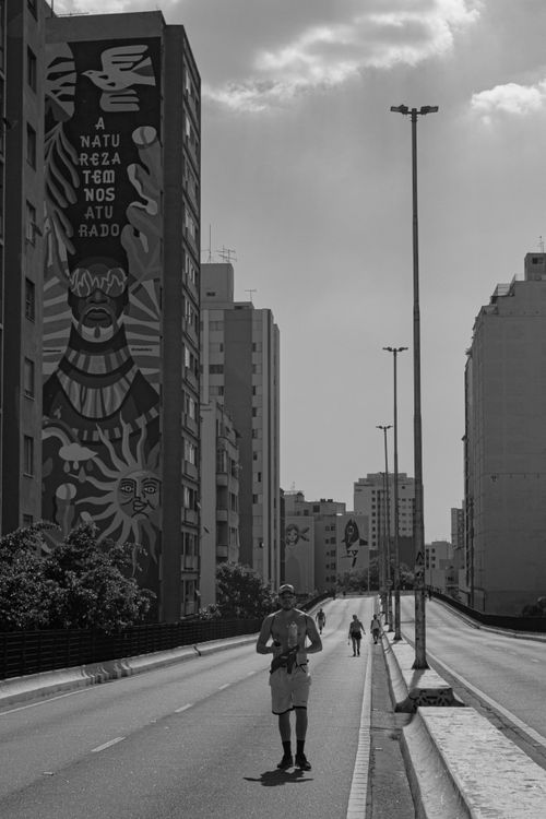 Free Monochrome cityscape featuring a striking mural and pedestrian on an empty street. Stock Photo