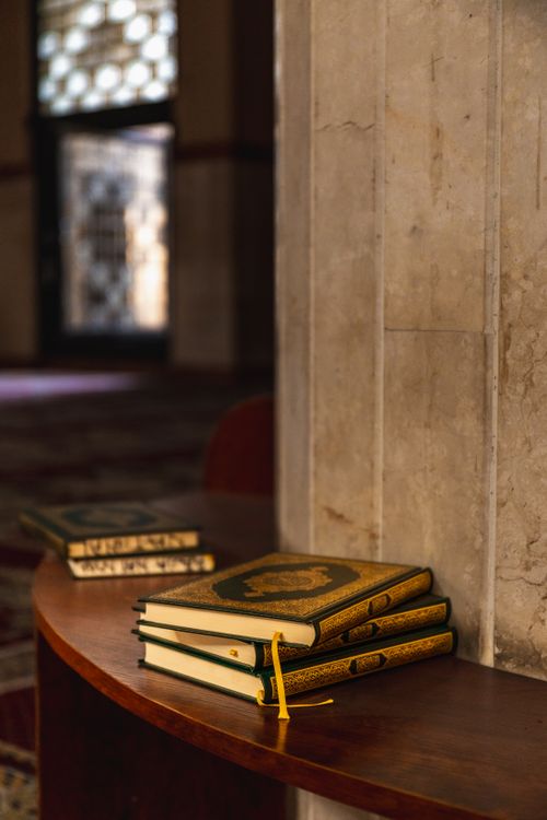 Free Stack of Quran books on a wooden shelf indoors at an Abuja mosque. Stock Photo