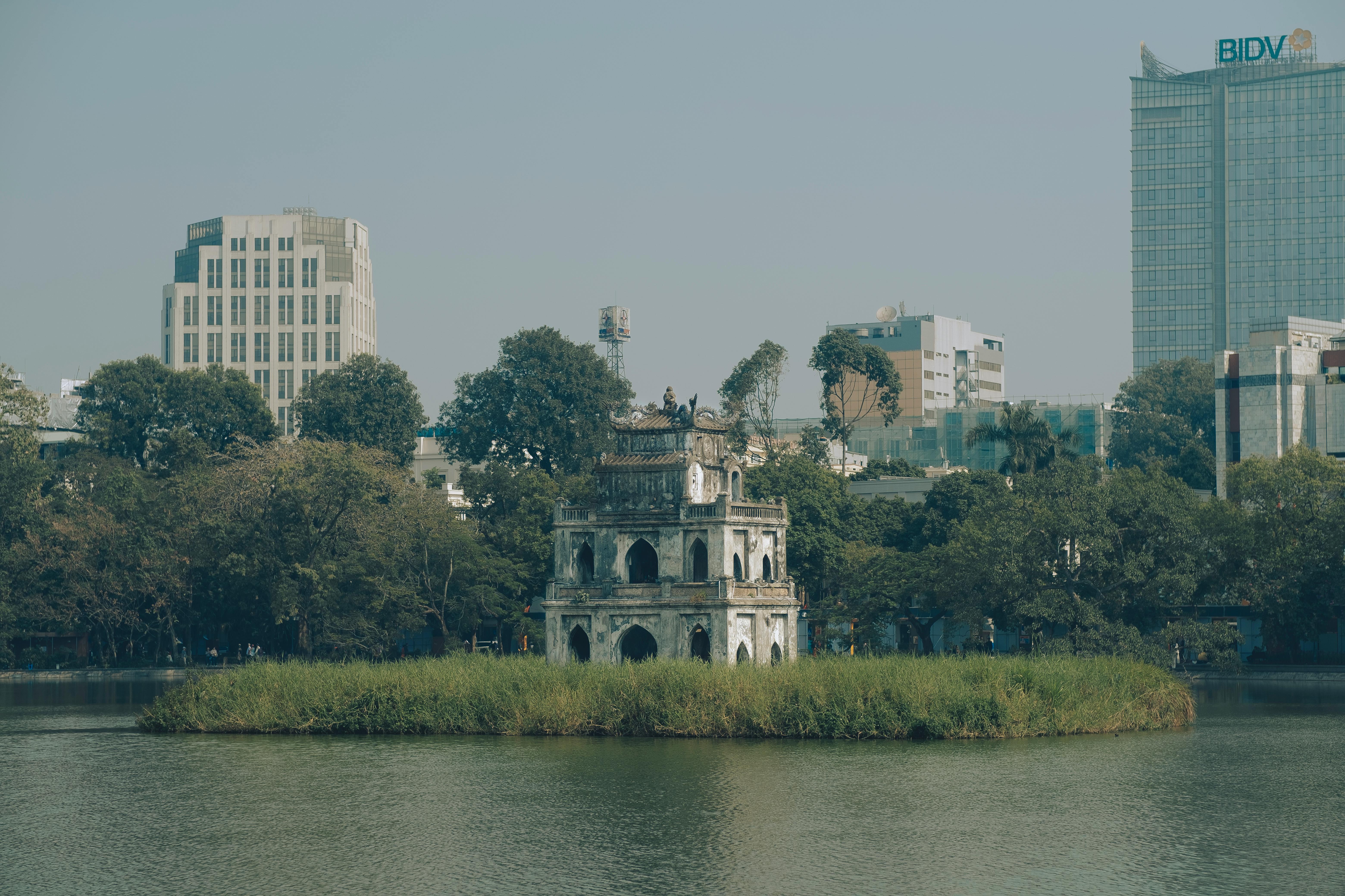 Scenic view of Turtle Tower in Hanoi's Hoan Kiem Lake surrounded by urban buildings.