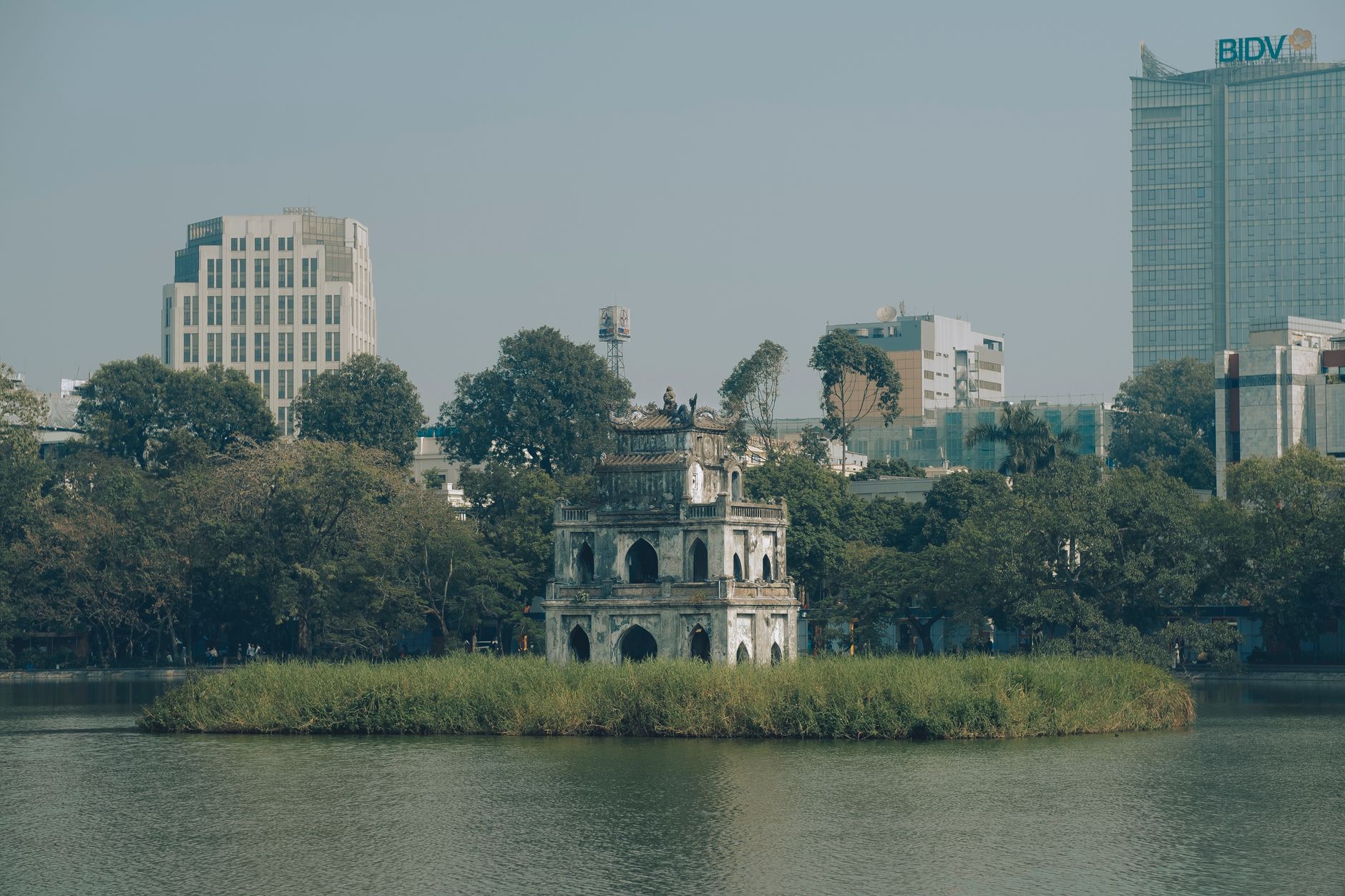 Scenic view of Turtle Tower in Hanoi's Hoan Kiem Lake surrounded by urban buildings.