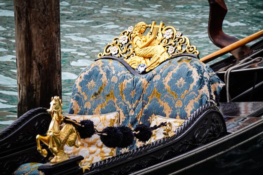 Close-up of a luxurious gondola seat in Venice adorned with ornate gold carvings and intricate fabric design.