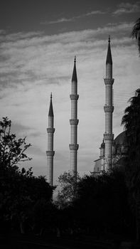 Black and white photo of minarets from a mosque silhouetted against a cloudy sky.