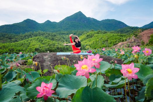 Woman practicing yoga on a rock surrounded by vibrant lotus fields in Hội An, Vietnam.