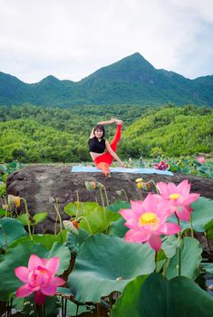 An adult practicing yoga on a rock surrounded by vibrant pink lotus blooms in Hội An, Vietnam.