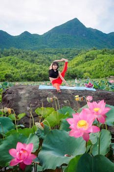 A woman practices yoga in vibrant lotus fields against a mountainous backdrop in Hội An, Vietnam.