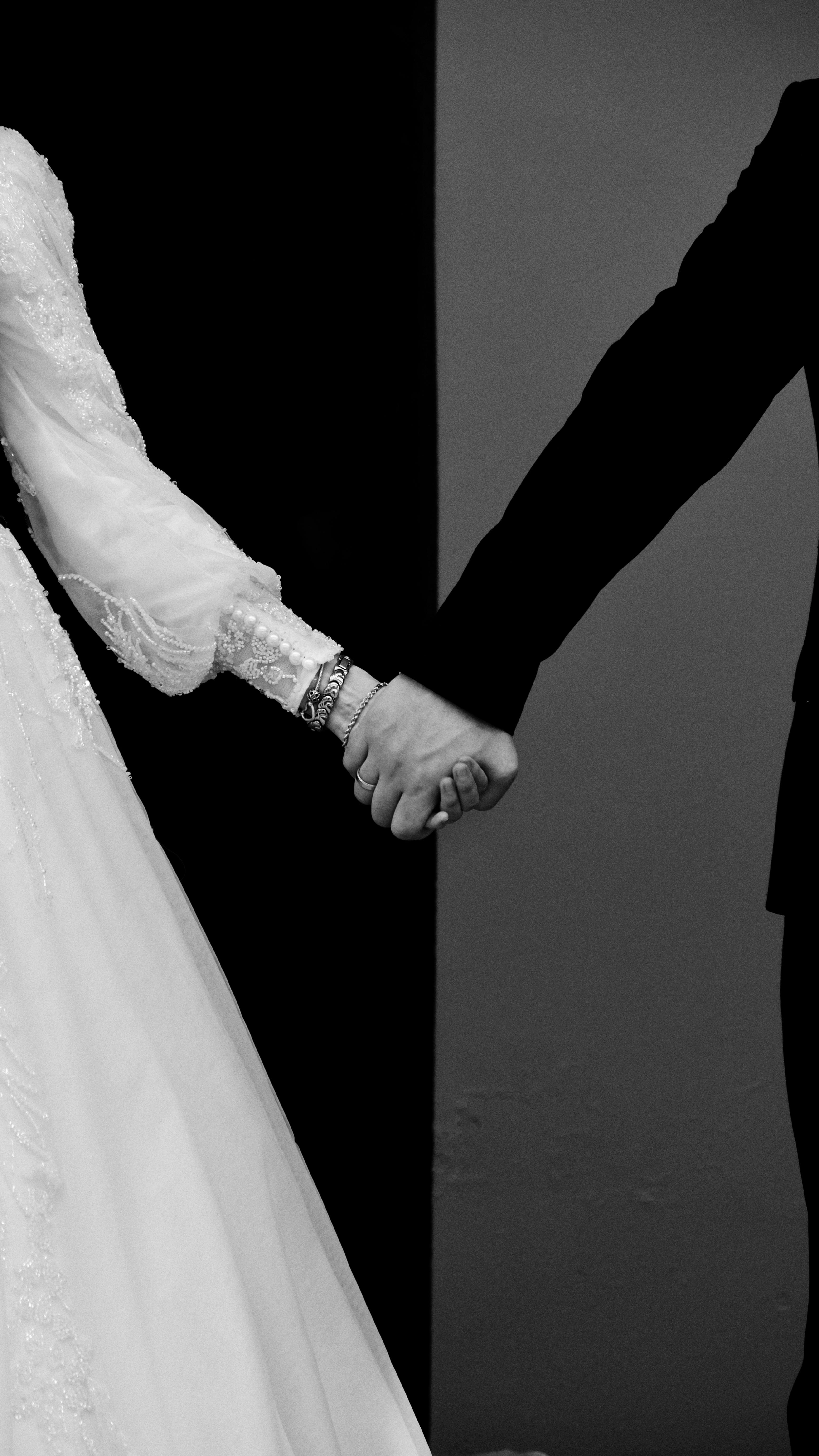 Black and white photo of a wedding couple holding hands, symbolizing unity and love.