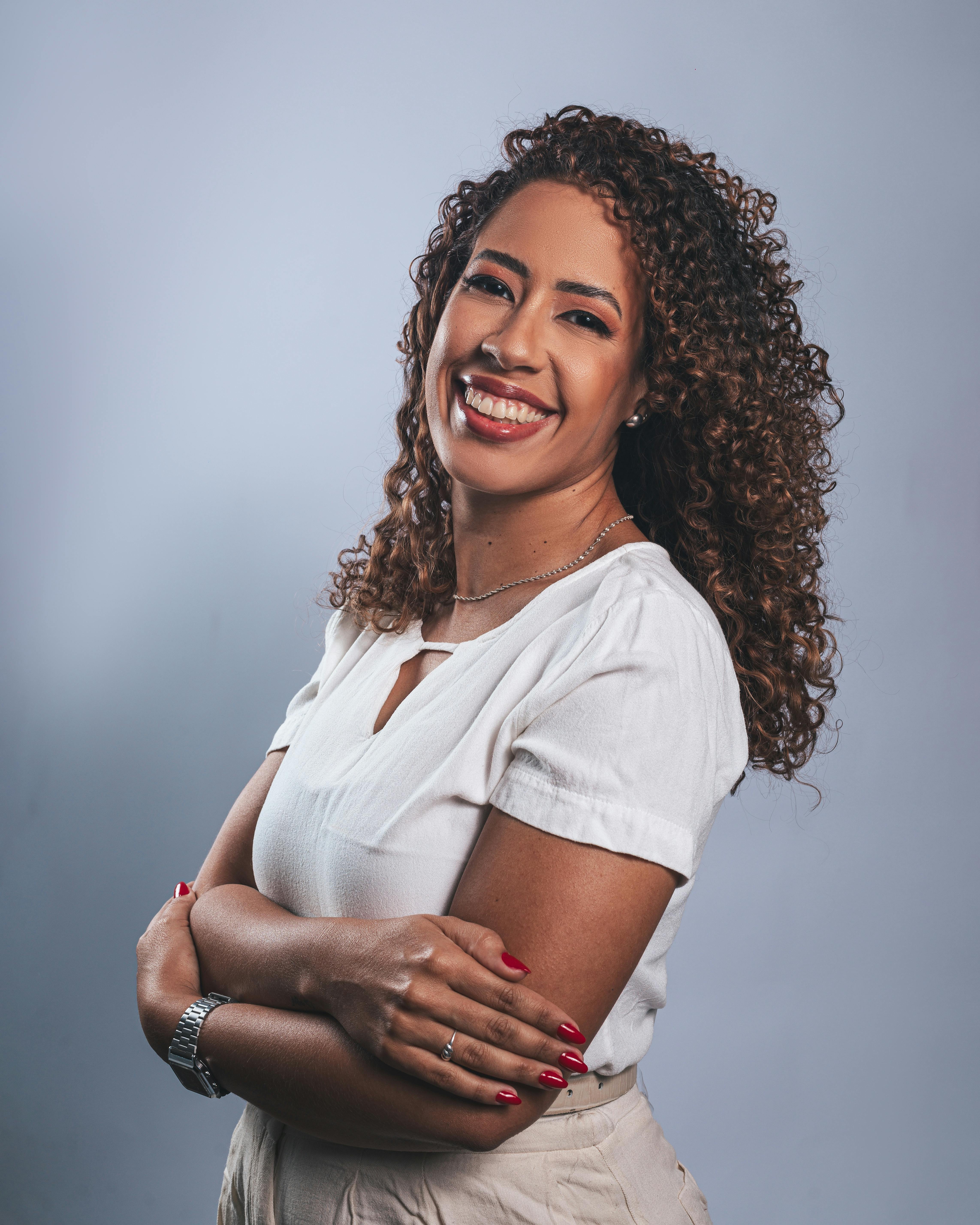 A cheerful woman with curly hair and a bright smile posing in a well-lit studio.