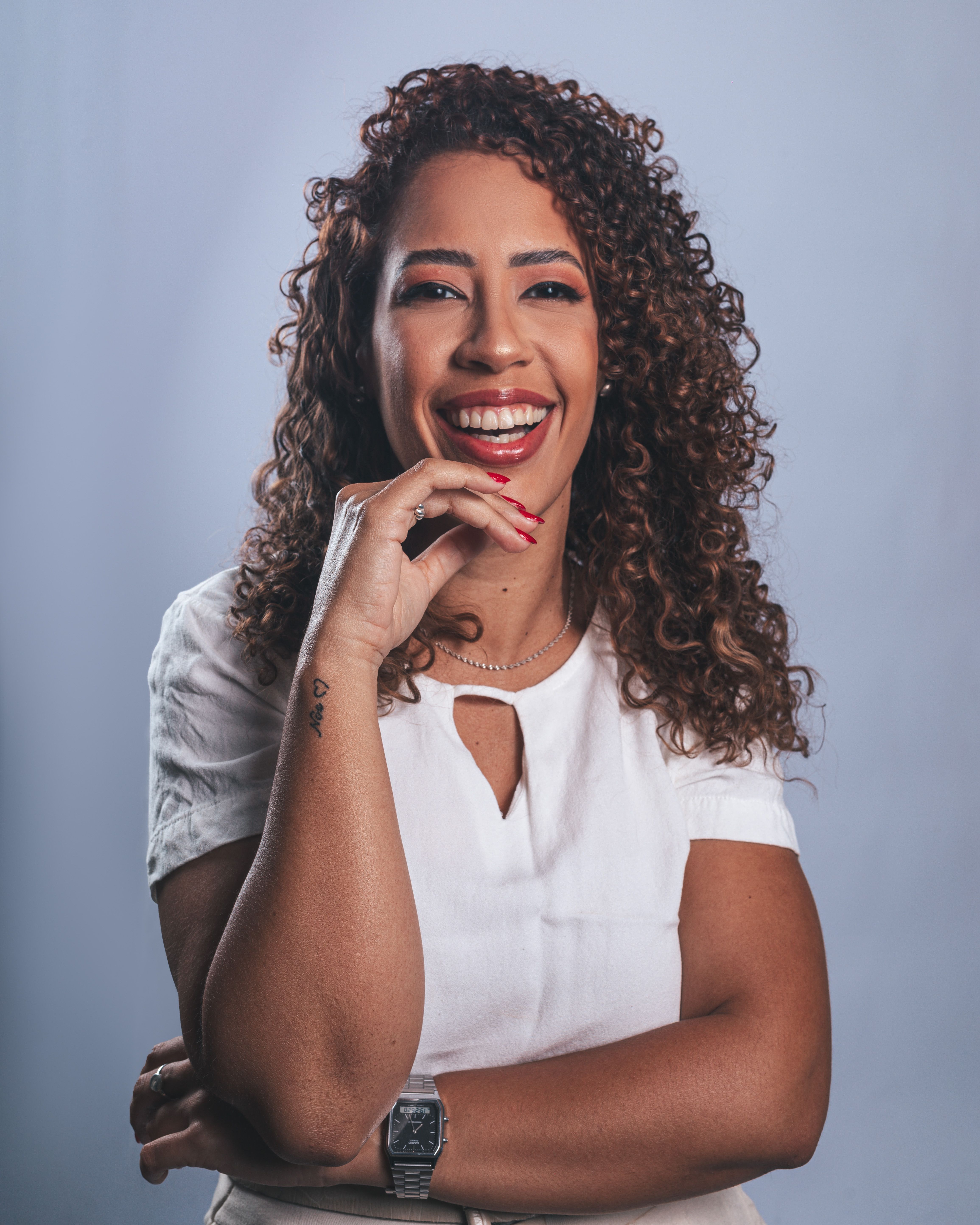 Portrait of a confident woman with curly hair smiling against a neutral background.