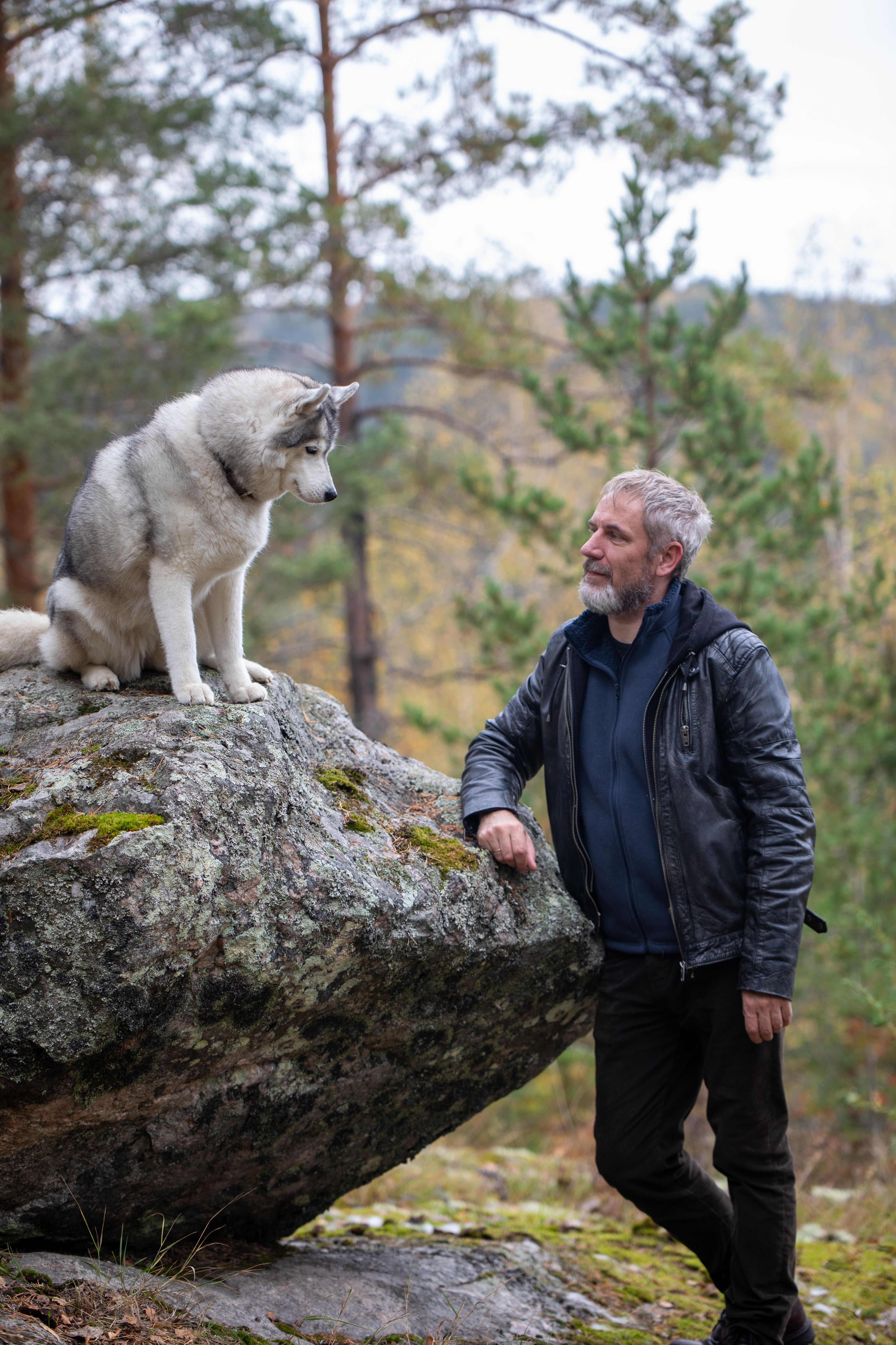 A man and his husky share a moment in a serene forest landscape.